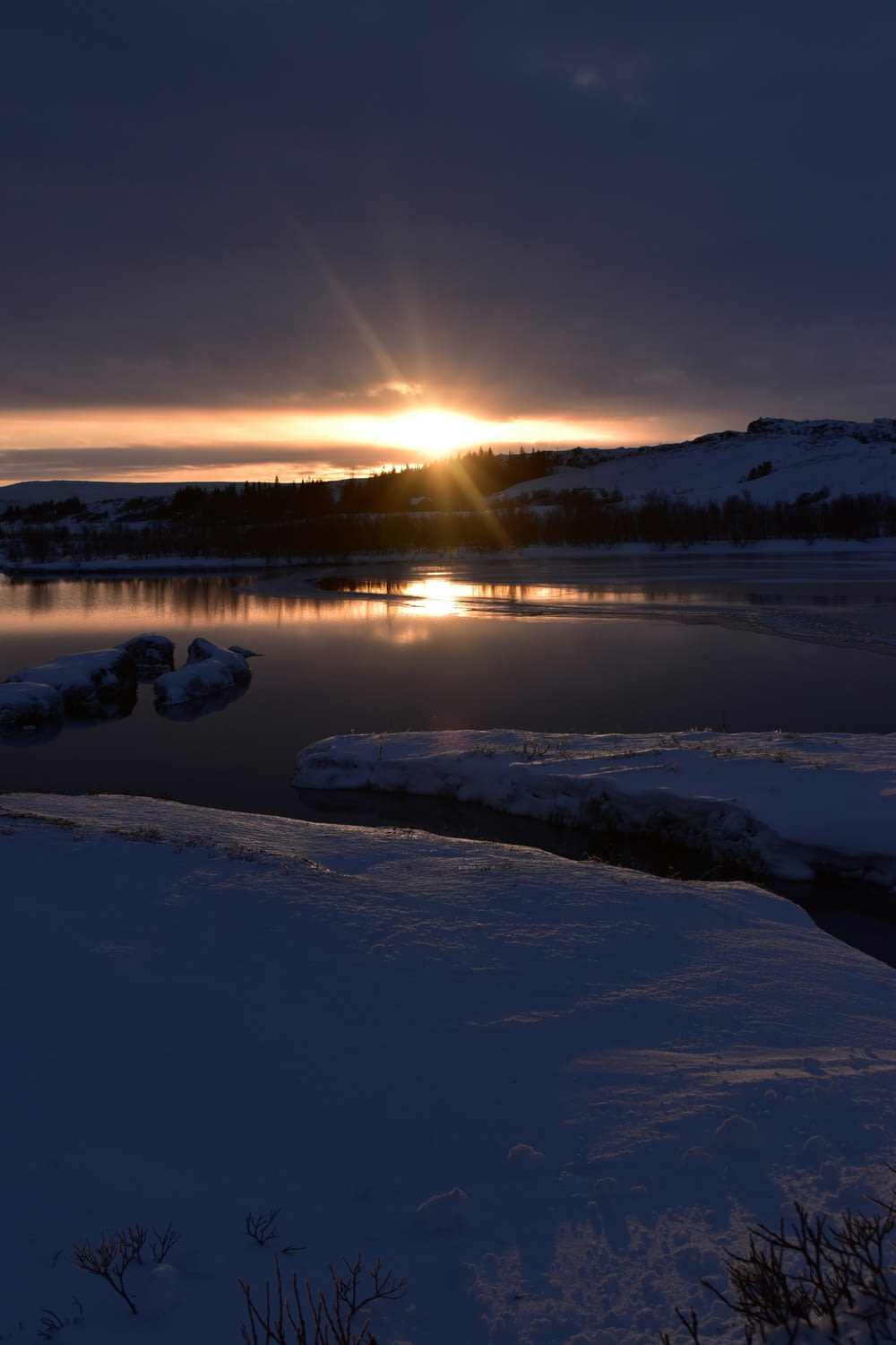 the sun is setting over a lake in the snow