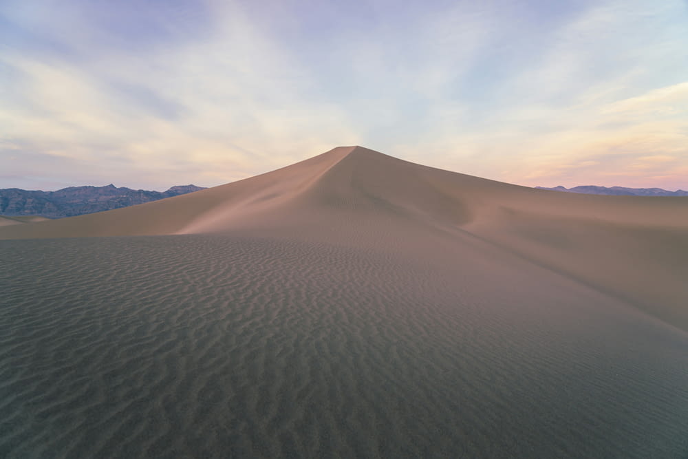 a large sand dune with mountains in the background