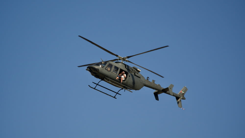 a military helicopter flying through a blue sky