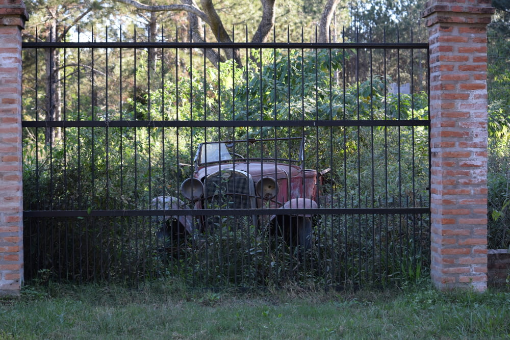an old car behind a fence in a field