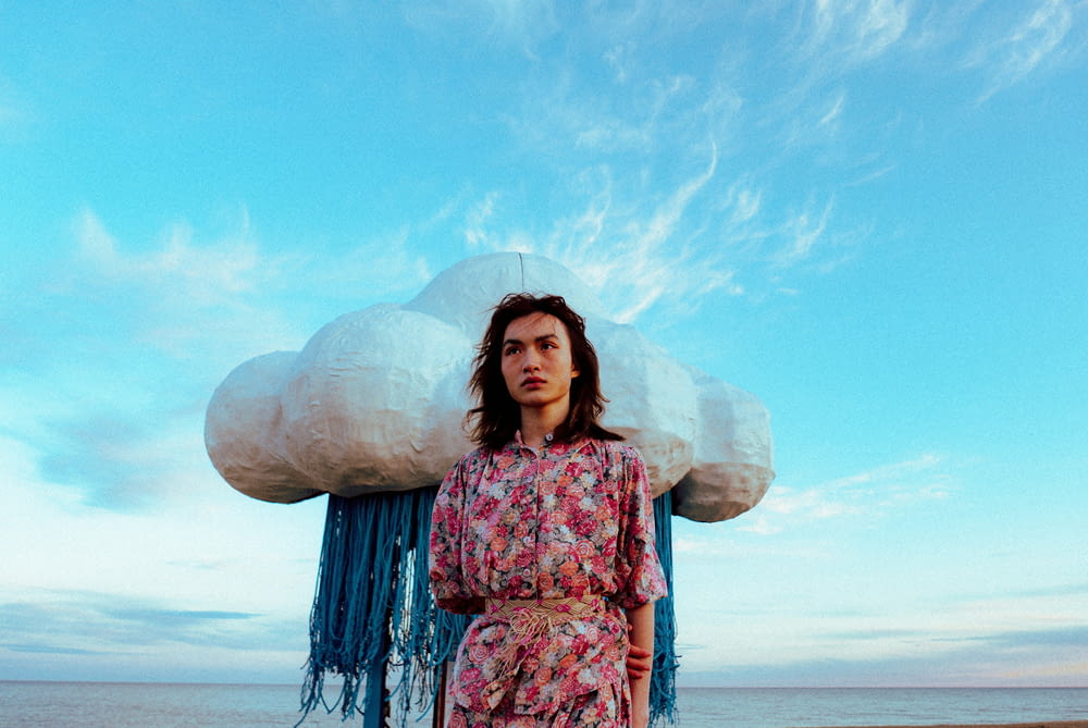 a woman standing on a beach with a large cloud above her head