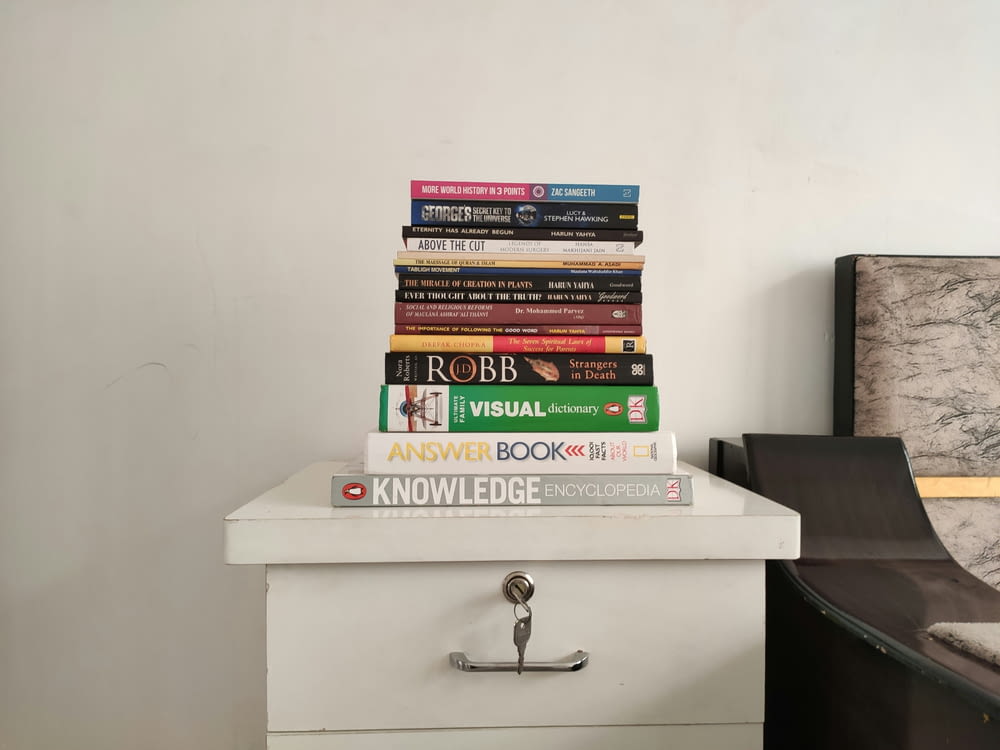 a stack of books sitting on top of a white dresser