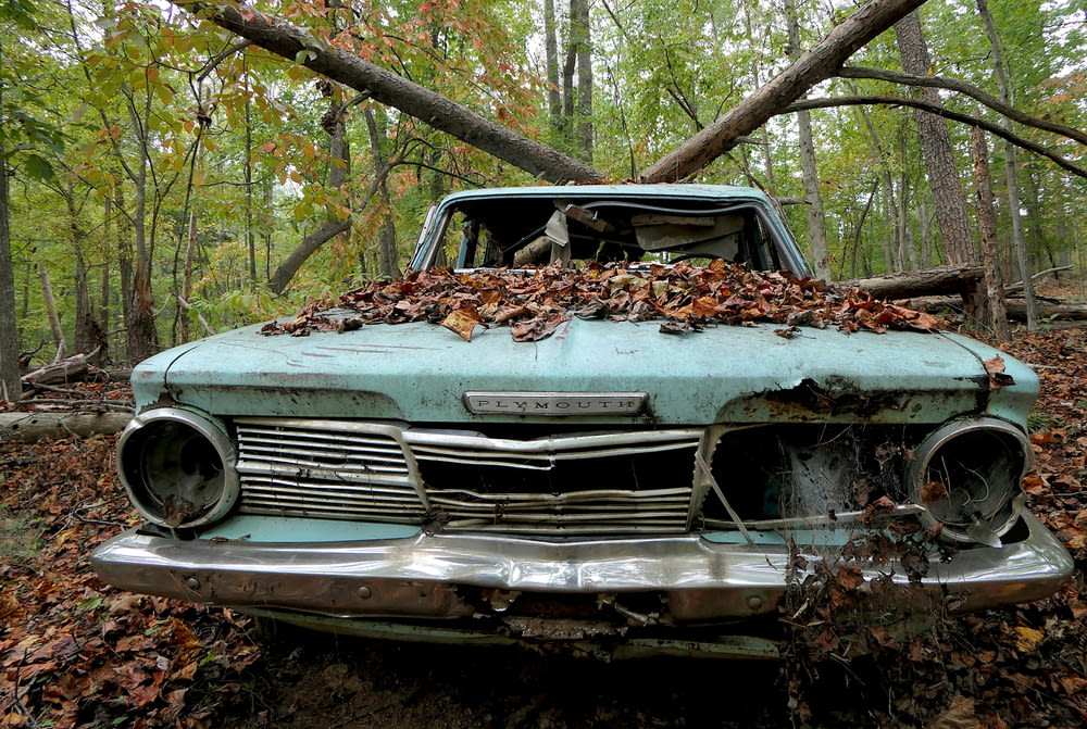 an old car is covered in leaves in the woods