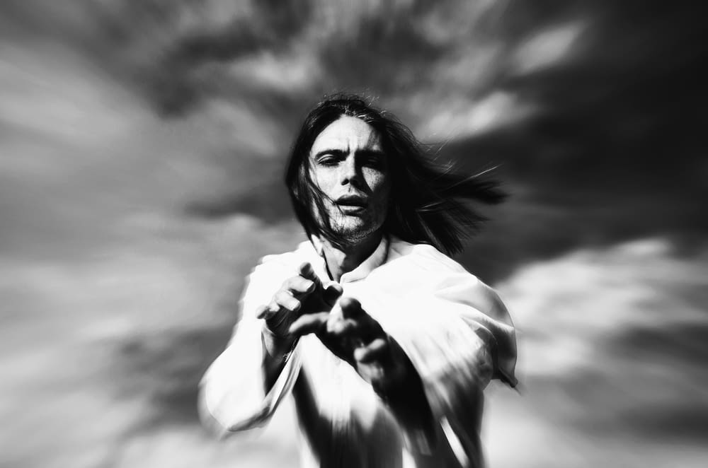 a man with long hair standing in front of a cloudy sky