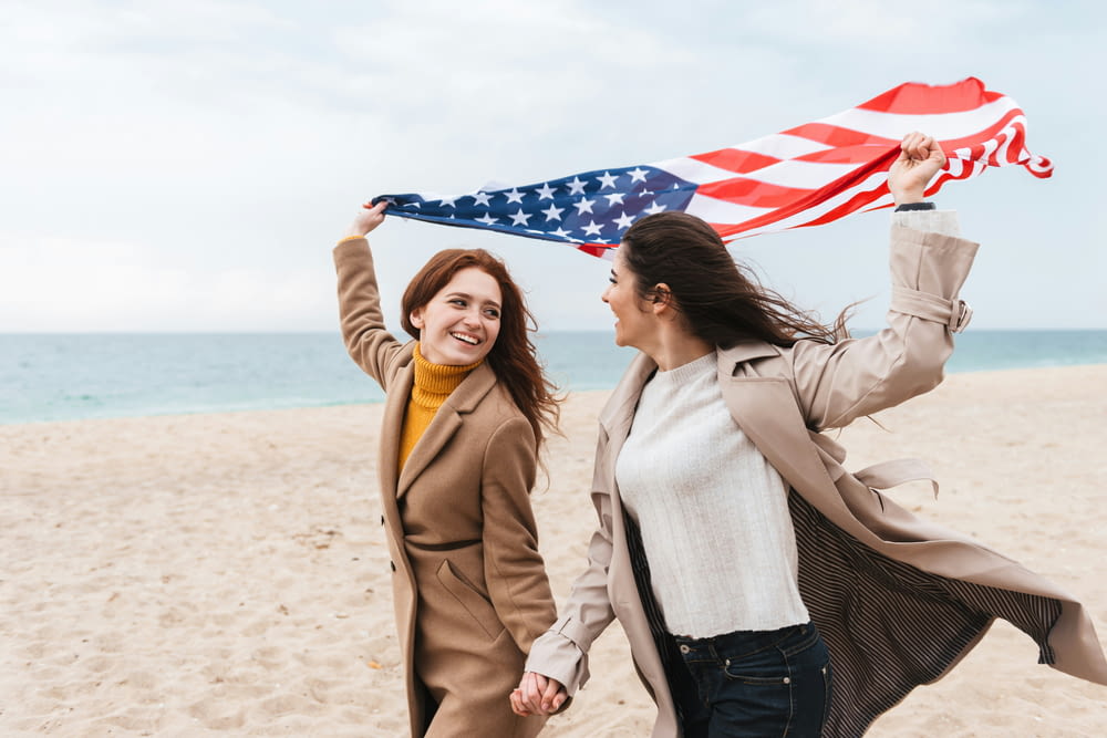 two women walking on a beach holding an american flag
