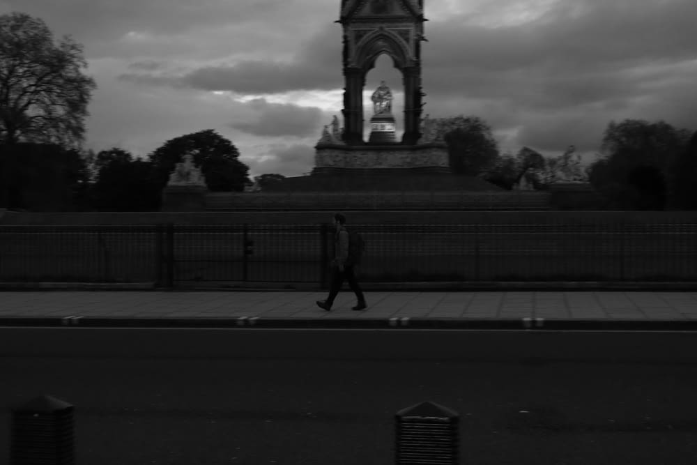 a black and white photo of a man walking in front of a clock tower