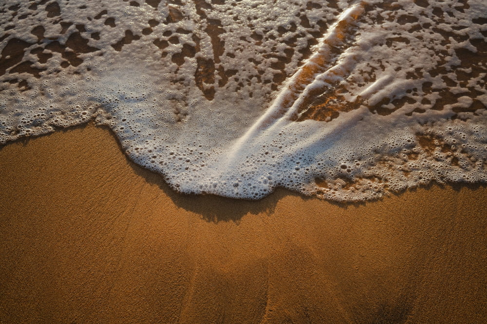 una playa de arena con una ola que llega a la orilla