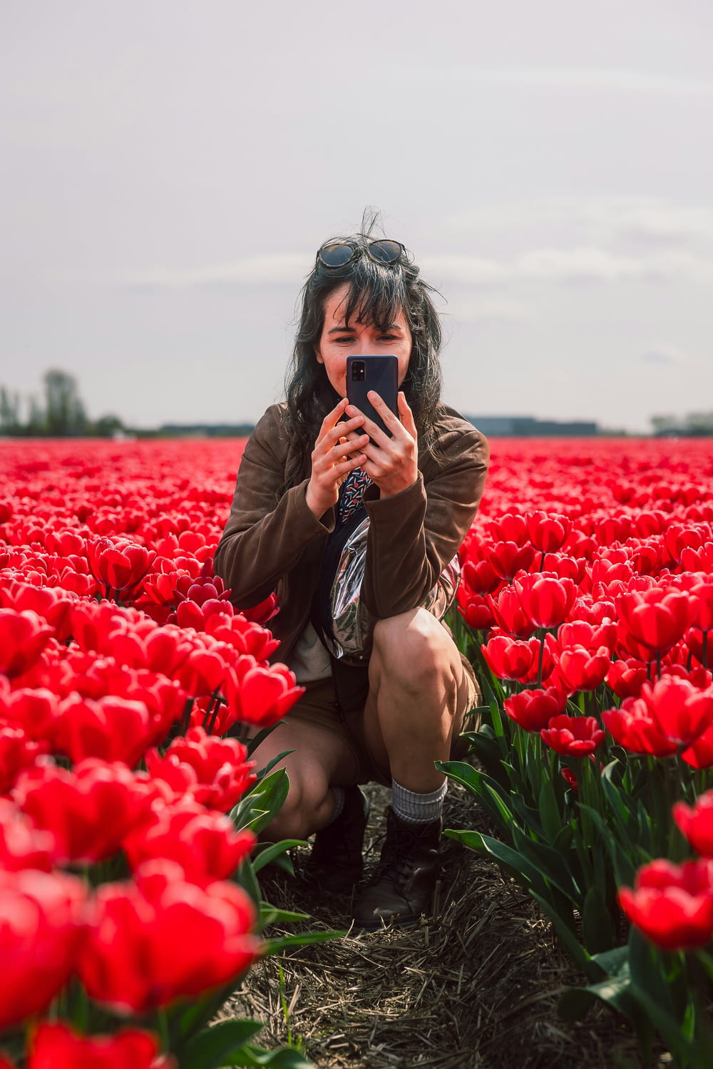 a woman taking a picture of herself in a field of red tulips