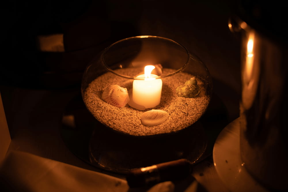 a lit candle in a bowl filled with sand and shells