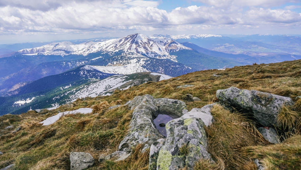 a view of a mountain range with rocks and grass in the foreground