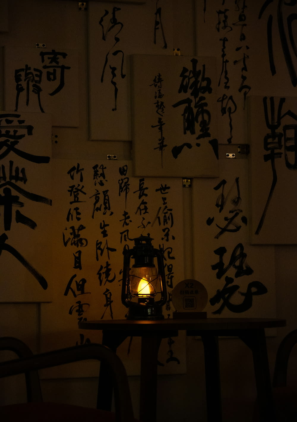 a table topped with a lit candle next to a wall covered in asian writing