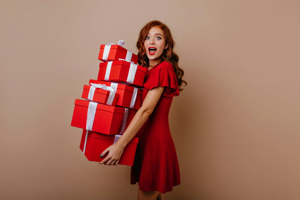 a woman in a red dress is holding a stack of presents