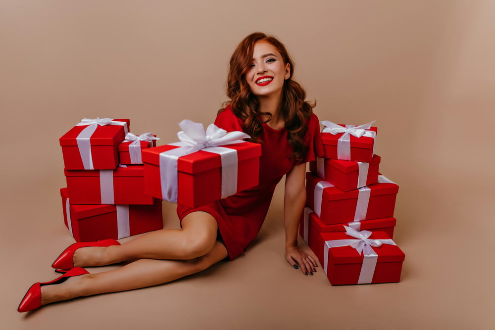 a woman in a red dress sitting on the floor with many wrapped presents