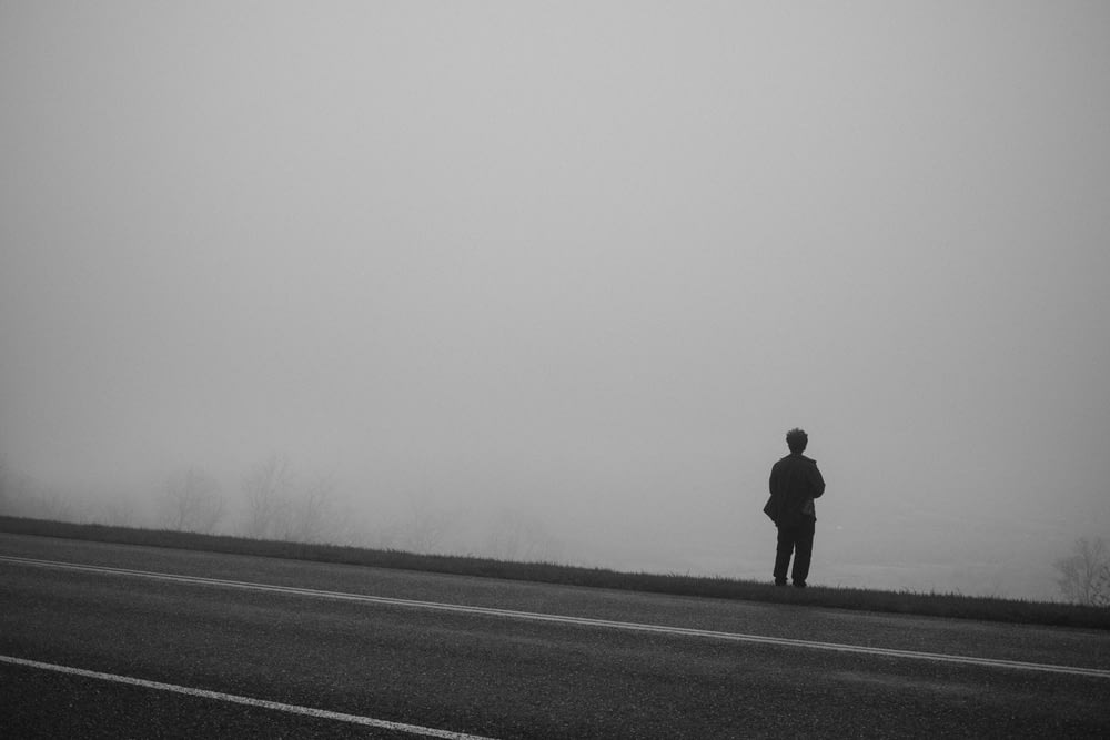 a man standing on the side of a road in the fog