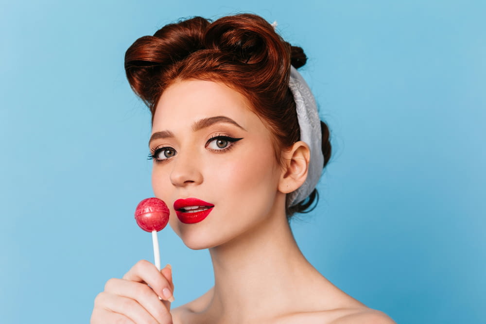 a woman with red lipstick holding a lollipop
