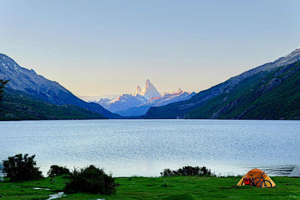 a tent is set up on the shore of a lake with mountains in the background