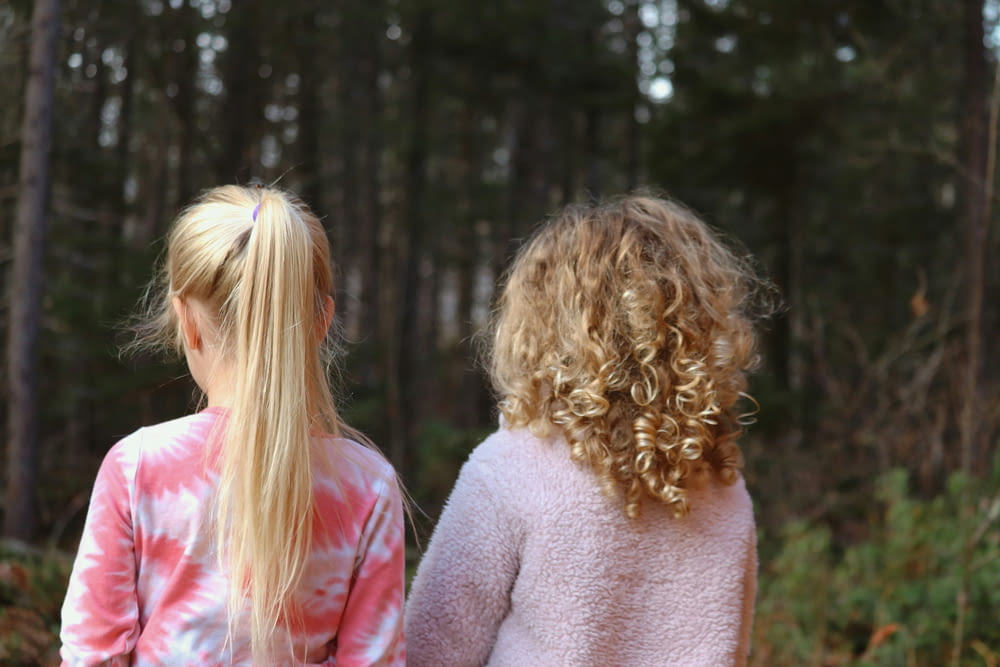 two little girls standing in the woods looking at something