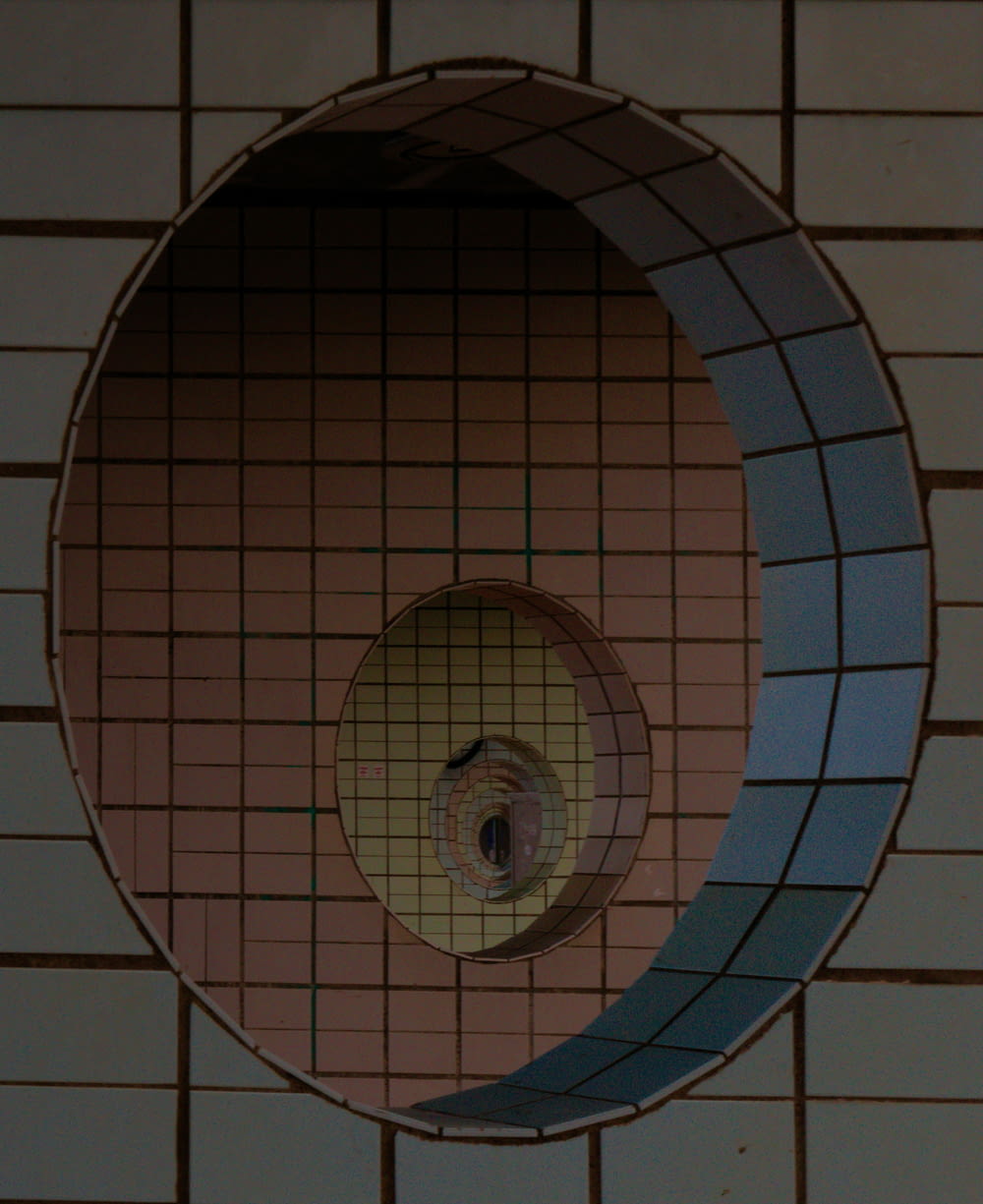 a round mirror on a tiled wall above a urinal