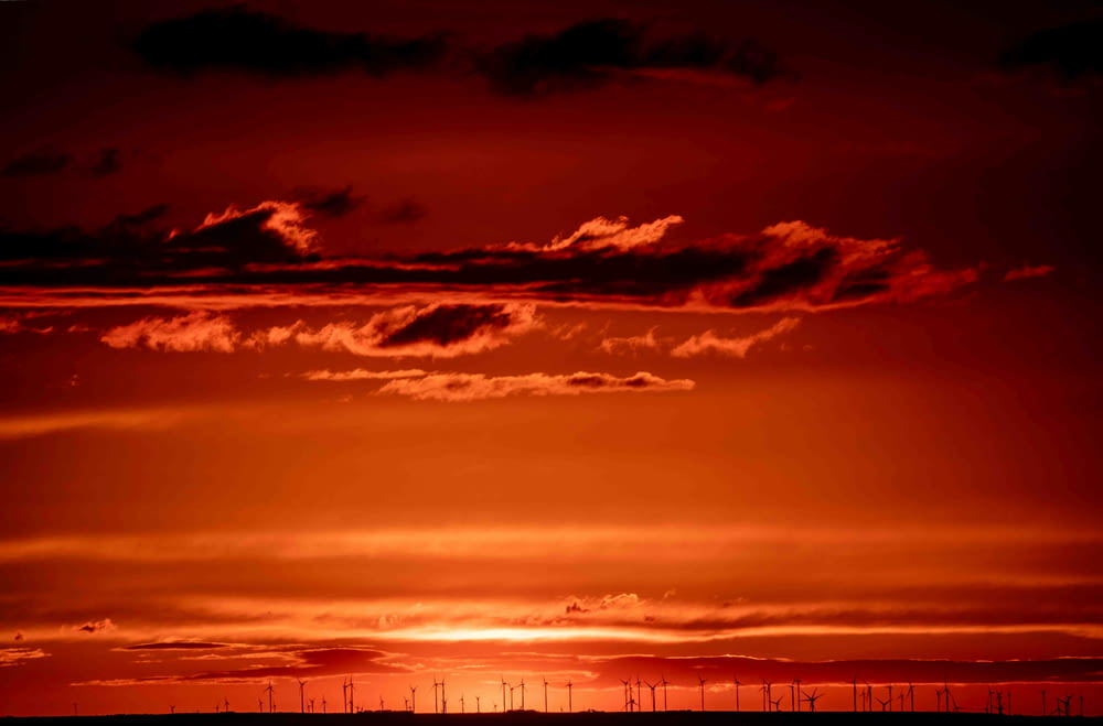 a red sky with a line of wind mills in the distance