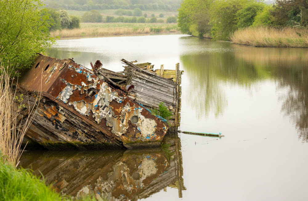 an old rusted boat sitting in the middle of a lake
