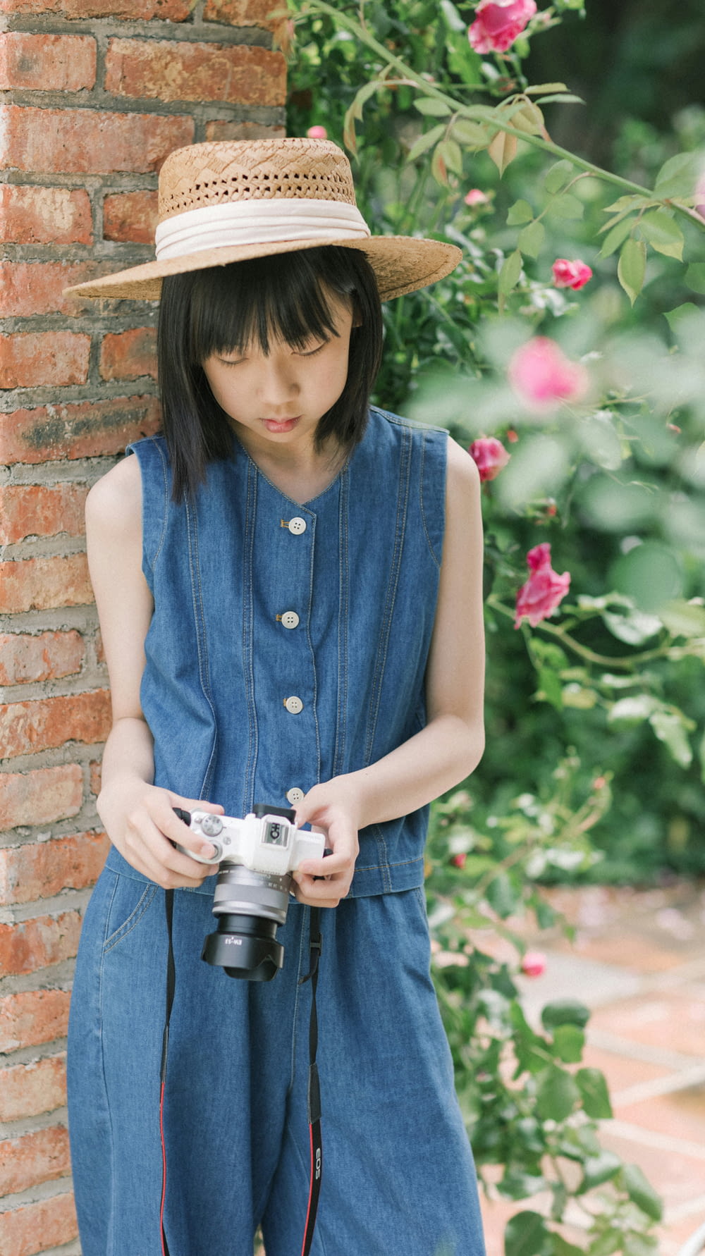 a girl in overalls and a hat holding a camera