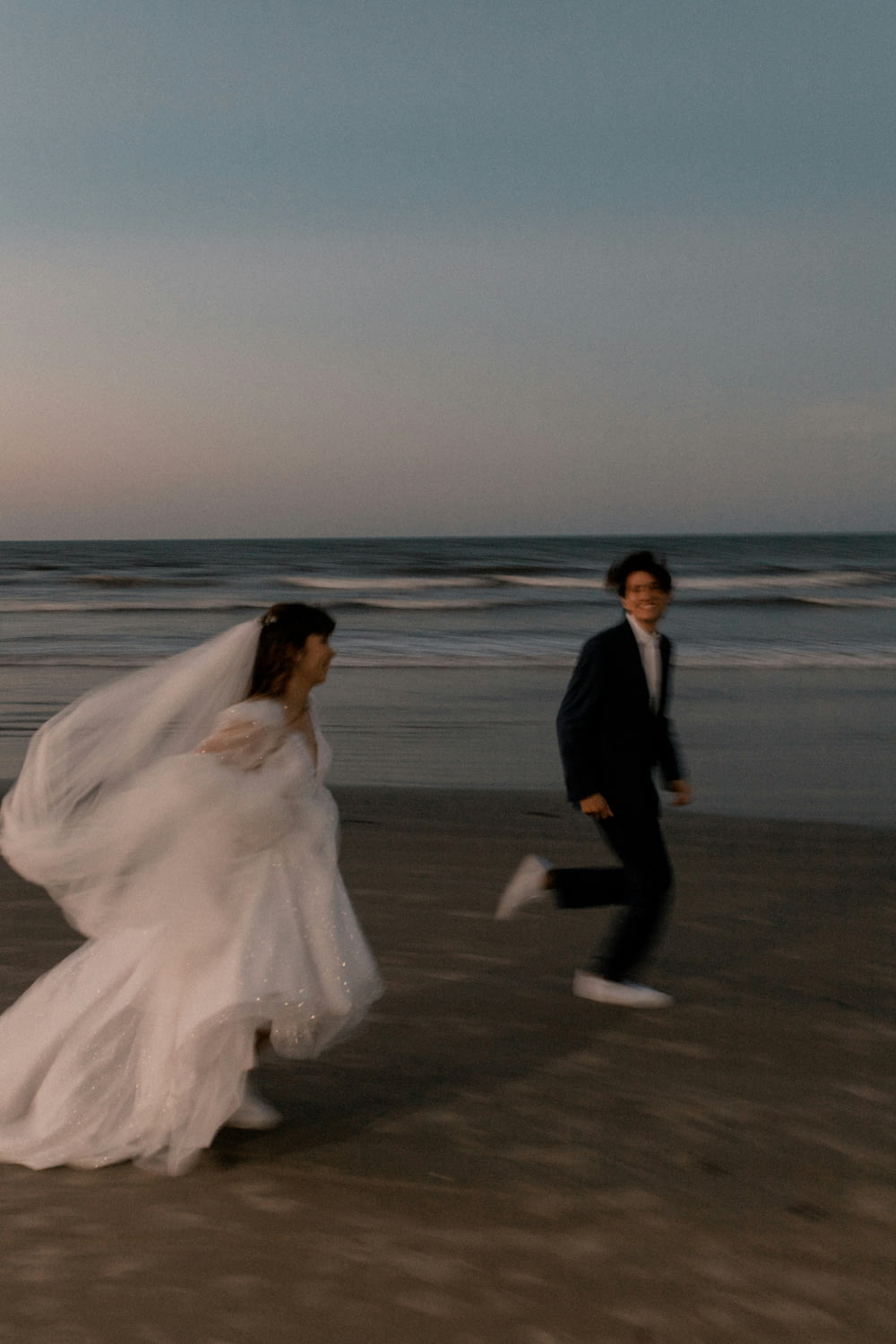 a bride and groom running on the beach