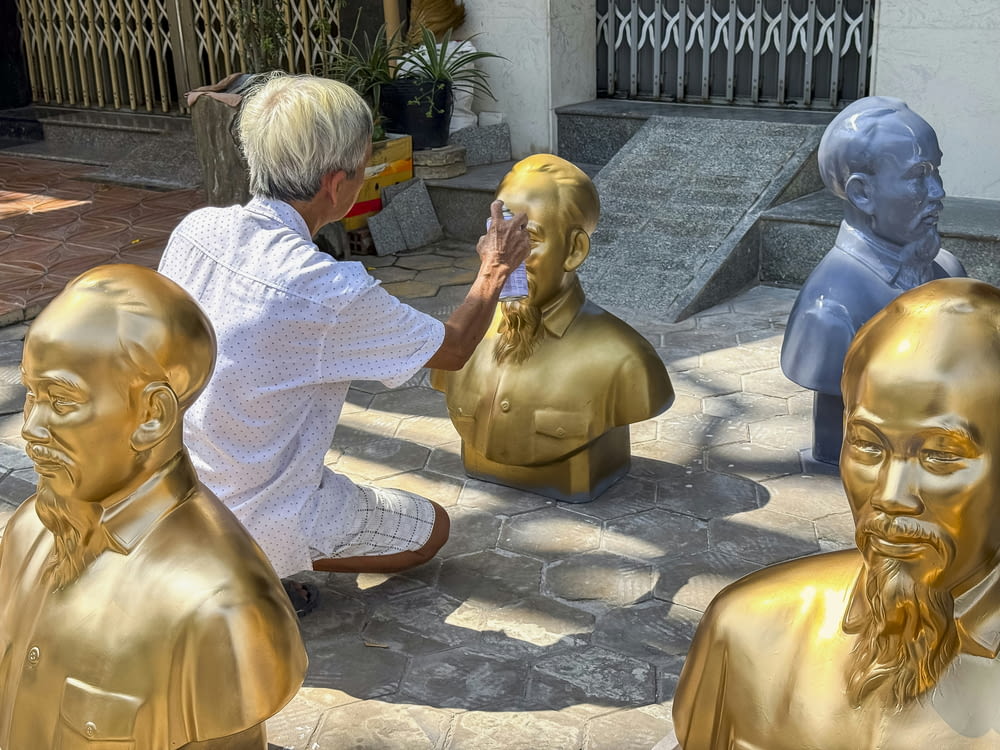 a man kneeling down next to a group of golden statues