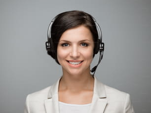 Belle femme souriante avec des écouteurs regardant la caméra du centre d’appels. Fond gris