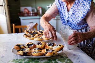 Ältere Frau backt Kuchen in ihrer heimischen Küche. Frisch gebackene Brötchen mit Puderzucker bestreuen.
