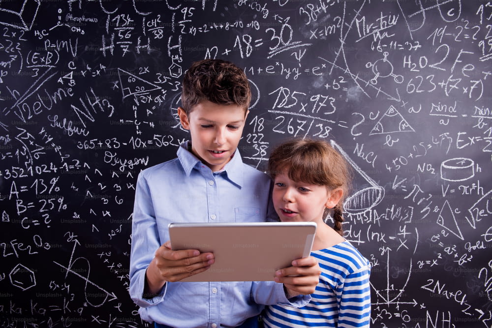 Süßer Junge und Mädchen mit Tablet in der Schule vor einer großen Tafel. Studioaufnahme auf schwarzem Hintergrund.