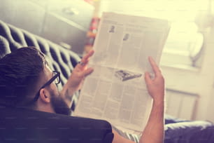 Männliches Model liegt auf einer Couch in einem Wohnzimmer und liest Zeitungen