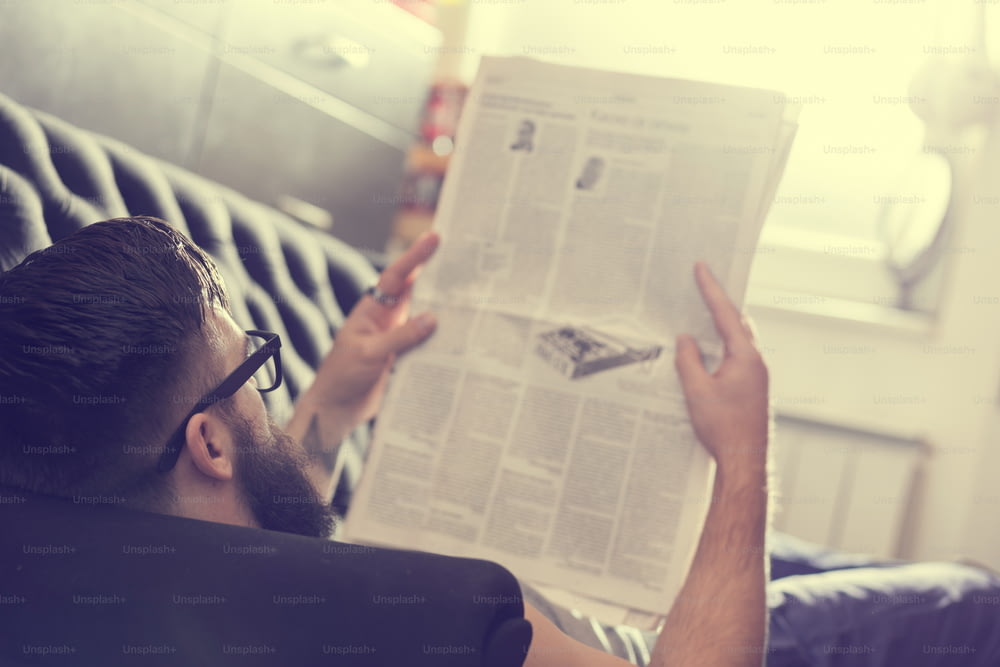 リビングルームのソファに横たわり、新聞を読む男性モデル