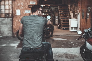 Vista posteriore di un giovane fiducioso seduto sulla sua moto con garage per moto sullo sfondo
