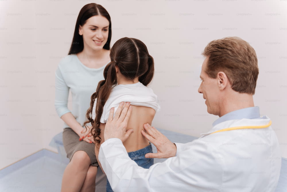 Back posture. Nice competent regular doctor running a checkup on girls spine and looking for a cause of scoliosis