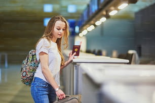 Belle jeune fille touriste avec un sac à dos et des bagages à main à l’aéroport international au comptoir d’enregistrement, donnant son passeport à un agent et attendant sa carte d’embarquement