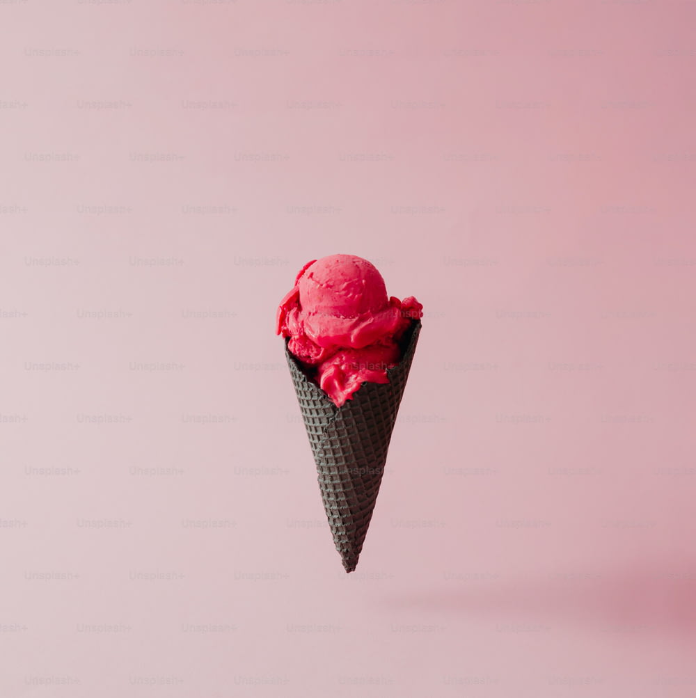 Glace à la fraise en cône noir sur fond rose pastel. Concept créatif d’été.
