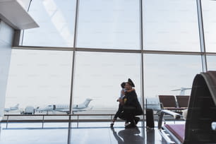 Aviator hockt und umarmt ein kleines Kind. Sie befinden sich in der Nähe der Glaswand am Terminal. Kopierbereich auf der linken Seite