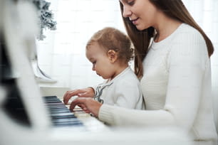 mother and daughter playing white piano, close up wiew.
