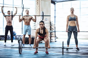 スポーティな筋肉質の人々のグループは、ジムで運動しています。ジムトレーニング。上半身裸のハンサムな男性と魅力的な女性がバーベルでエクササイズをしています。重量挙げ。