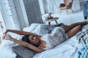 Mujer joven atractiva sonriendo y estirándose mientras está acostada en la cama en casa
