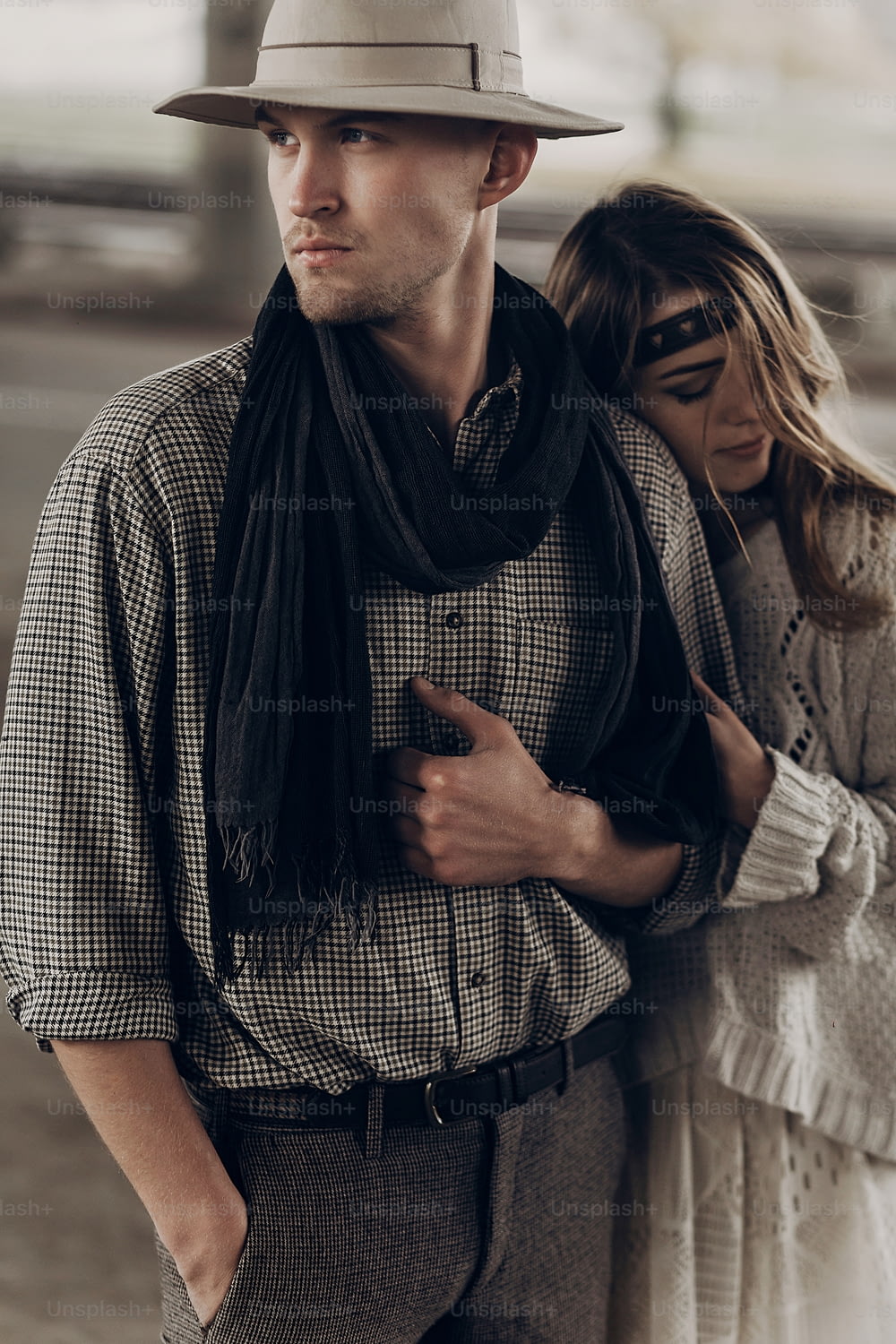 Romantic gypsy woman in stylish boho clothes and white dress hugging handsome cowboy man in white hat and scarf