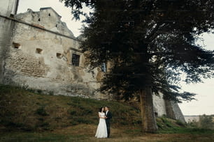 Stilvolle Luxus-Braut und Bräutigam posieren zusammen in der Nähe von Old Castle bei Sonnenuntergang. Glücklicher Moment des schönen Hochzeitspaares im Freien