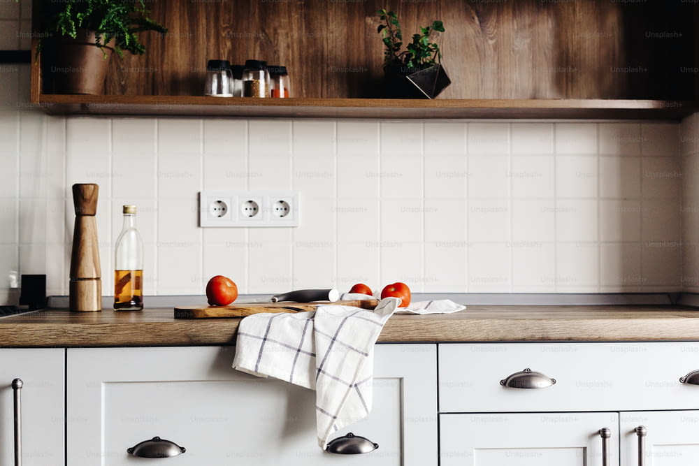 wooden board with knife, tomatoes , olive oil on modern kitchen countertop and shelf with spices and plants. cooking food. Stylish kitchen interior design in scandinavian style, steel appliances