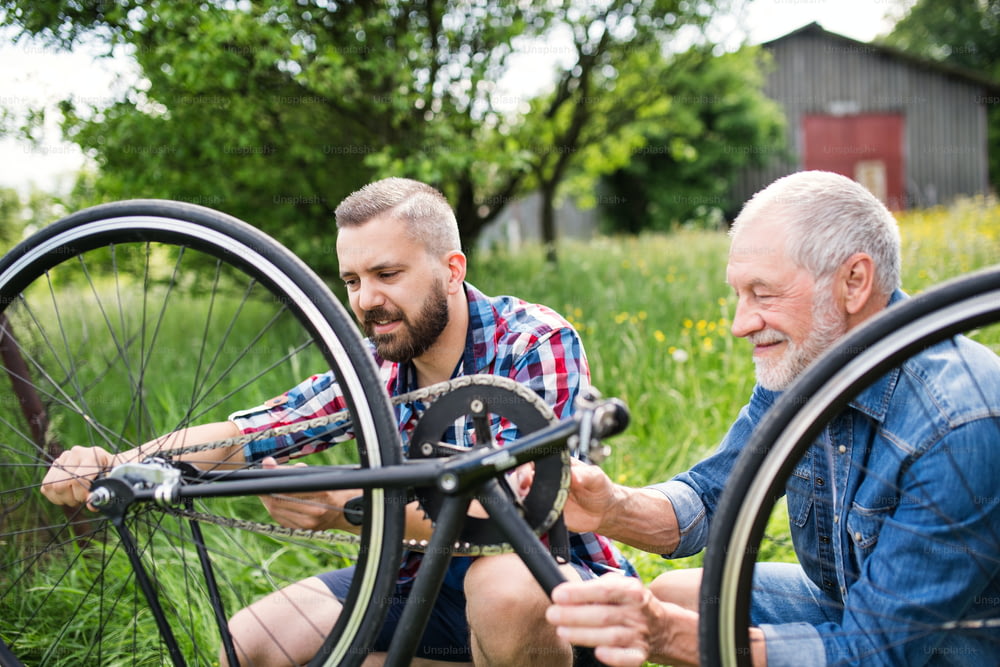 Um filho hipster adulto e pai sênior consertando bicicleta do lado de fora em um dia ensolarado de verão.