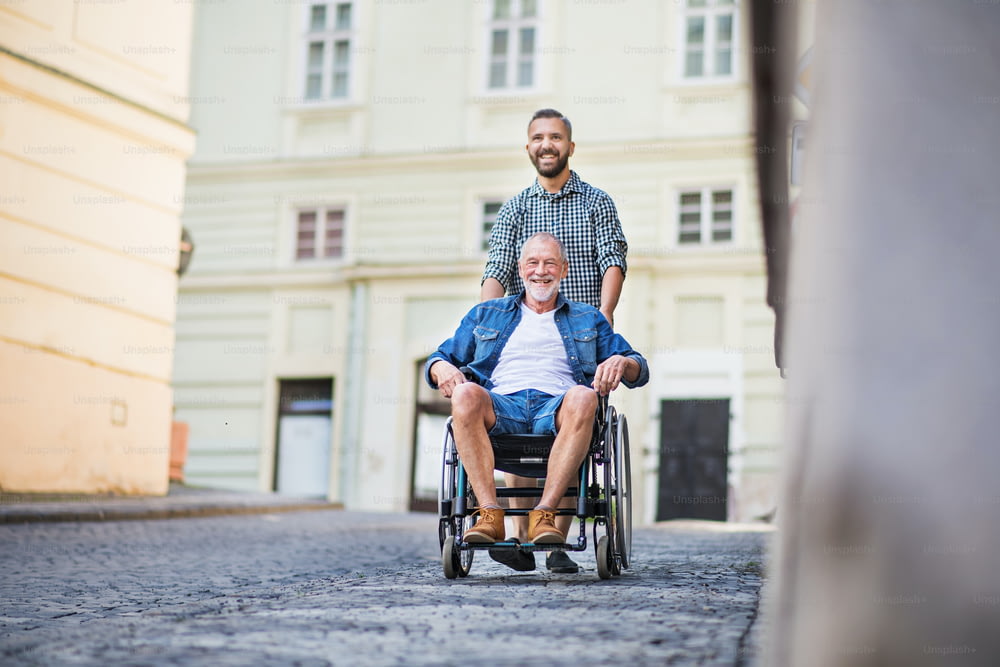 Un fils hipster adulte avec son père aîné en fauteuil roulant lors d’une promenade en ville.