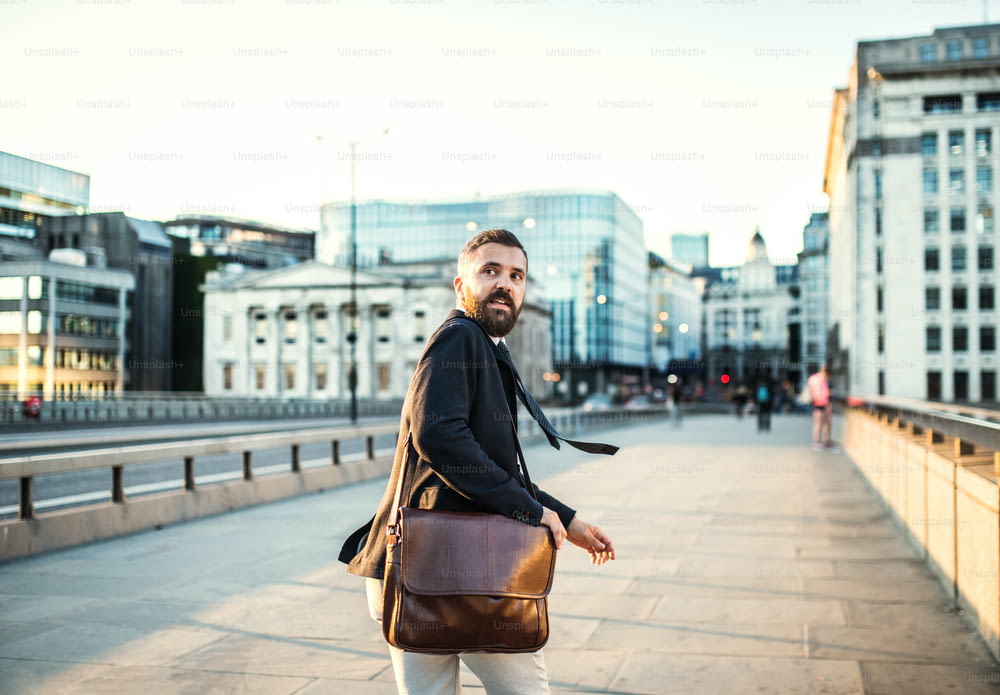 Vue arrière d’un homme d’affaires hipster avec un sac courant dans la rue de la ville, regardant en arrière.