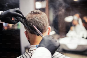 A rear view of man client visiting haidresser and hairstylist in barber shop.