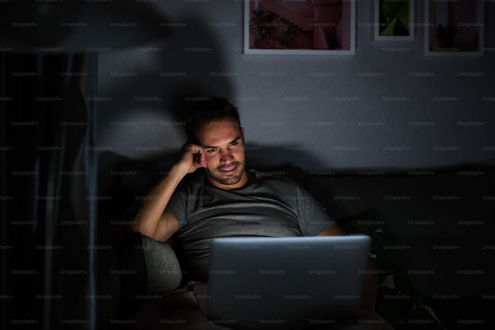 Man sitting on the sofa in the dark in pajamas with a computer