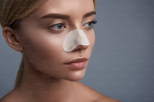 Calm thoughtful young woman looking into the distance while using convenient nose pore strip