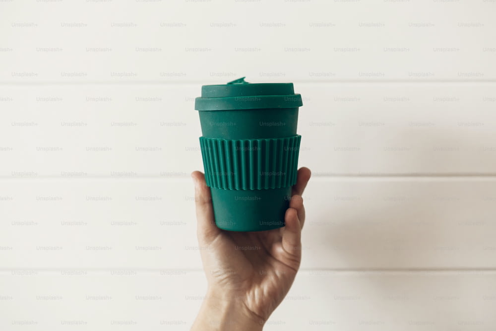 Ban single use plastic. Hand holding stylish reusable eco coffee cup on white wooden background. Green Cup from natural  bamboo fiber, zero waste concept. Make a choice. Take away coffee